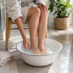 Pour évoquer le soulagement doux d’un pied qui brûle, une personne rafraîchit ses pieds dans une bassine d’eau claire.
